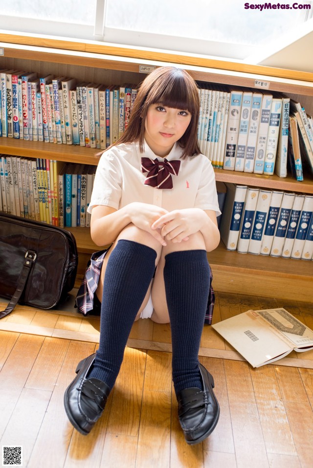 A woman sitting on the floor in front of a bookshelf.