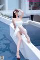 A woman in a white dress sitting on the edge of a pool.