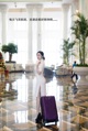 A woman in a white dress with a purple suitcase.