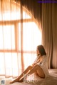 A woman sitting on a bed in front of a window.