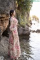 A woman in a long dress standing by the water.