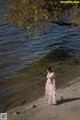 A woman in a long dress standing by the water.