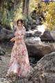 A woman in a long dress standing by a stream.