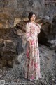 A woman in a long dress standing in front of a rock.