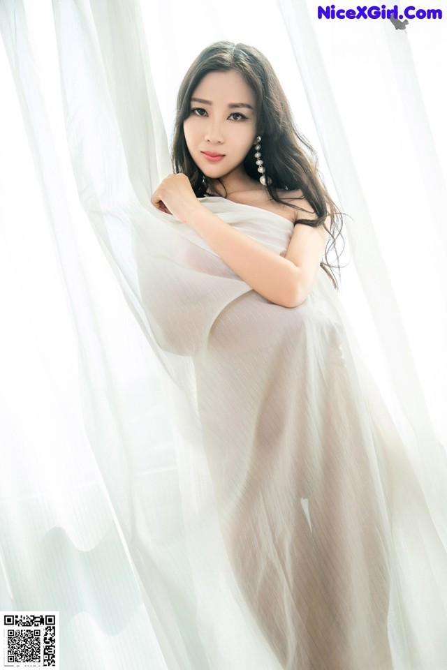 A woman in a sheer white dress posing for a picture.