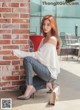 A woman sitting on the ground next to a brick wall.