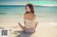 A woman sitting on the beach in a bikini.