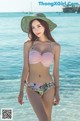 A woman in a bikini and hat standing in the water.