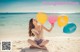 A woman sitting on the beach holding a bunch of balloons.