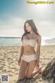 A woman in a white bikini sitting on a beach.