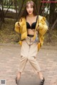 A woman in a yellow jacket and beige pants posing on a swing.