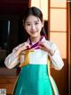 A woman in a green and white hanbok is posing for a picture.