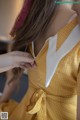 A woman in a yellow and white checkered dress is adjusting her hair.