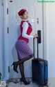 A woman in a red hat and striped skirt with a suitcase.