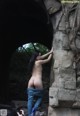 A naked woman standing in front of a stone wall.