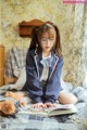 A girl sitting on a bed reading a book.