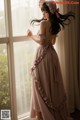 A woman in a pink dress standing by a window.