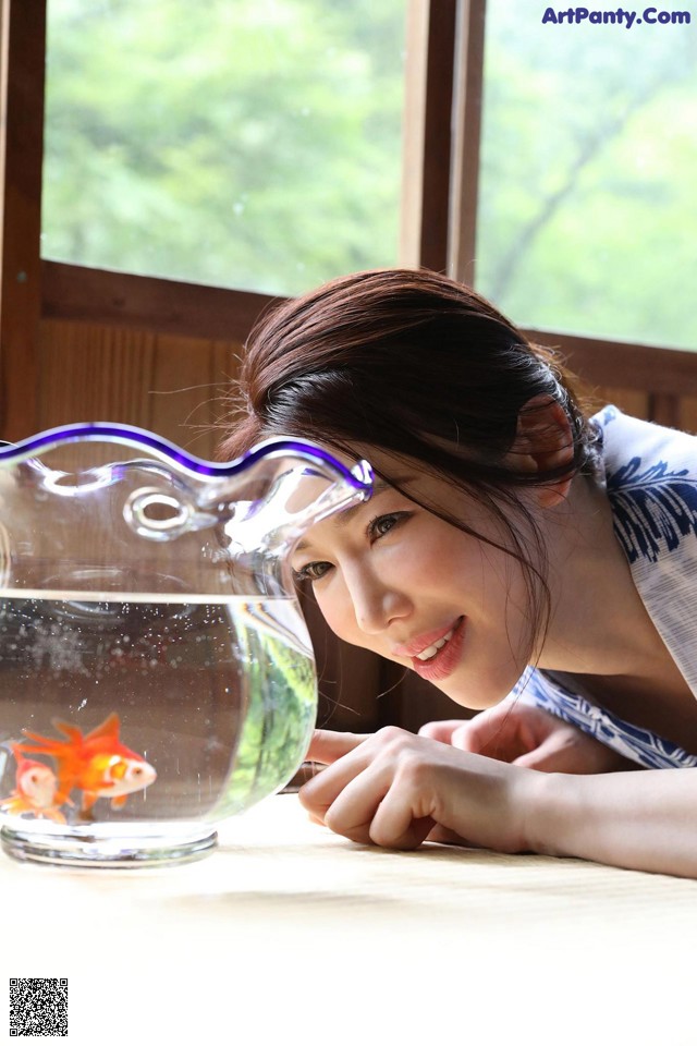 A woman looking at a goldfish in a fish bowl.
